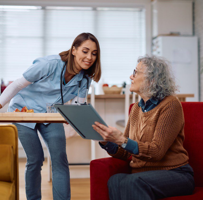 GettyImages-2207786746 Nurse assisting elderly woman with tablet.