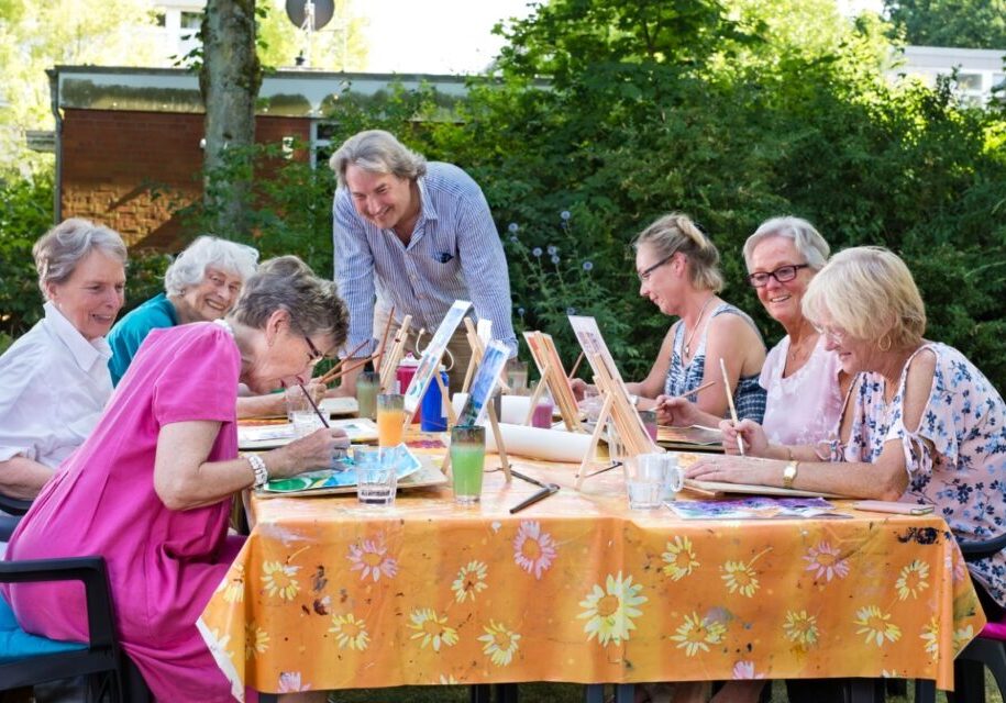 Group of seniors painting outdoors at table.