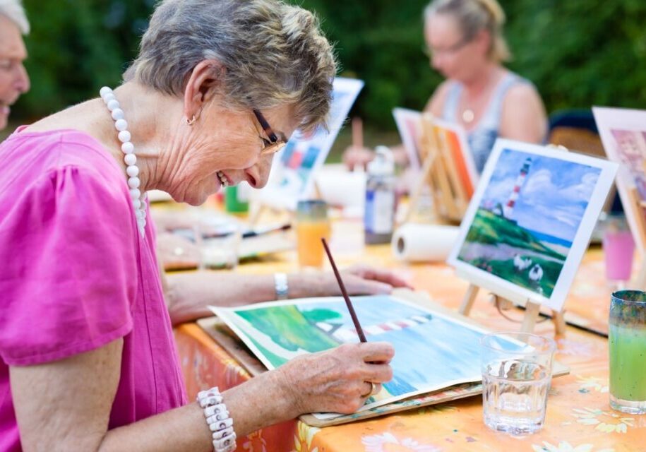 Elderly women painting outdoors at a table.
